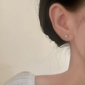 Close-up of minimalist round white pearl stud earrings worn by a model in soft lighting
