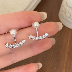 Detail of silver pearl and zircon earrings held by hand showing the dual-wear style