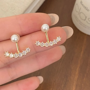 Macro detail of gold earrings featuring white pearls and sparkling zirconia stones
