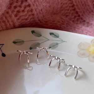 Elegant silver bow stud earrings set displayed on a porcelain plate with pink background
