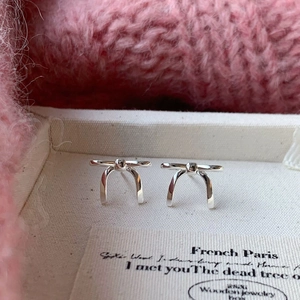 Macro shot of silver bow stud earrings on a jewelry tray with soft pink knit background