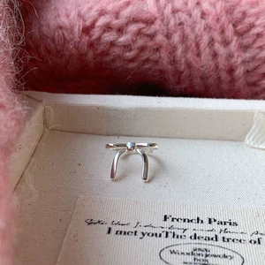 Close-up of a delicate silver bow ring placed inside a beige fabric jewelry gift box