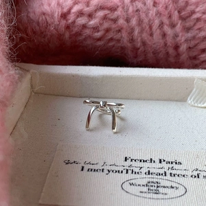 Macro shot of silver bow stud earrings resting in a beige canvas jewelry box with soft fabric