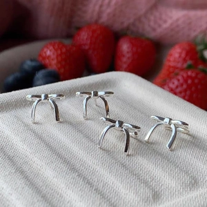 Macro detail of polished S925 silver bow stud earrings on a textured display pad