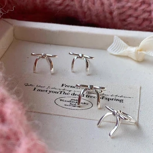 Close-up of silver bow stud earrings on a cream-colored textured jewelry display tray