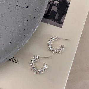 Silver C-shaped hoop earrings with faceted textured finish on a minimalist background