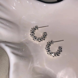 Detail of silver C-shape stud earrings with intricate woven metal texture on white ceramic