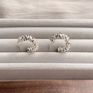Detail of silver C-shaped earrings with irregular crushed texture on a grey velvet box