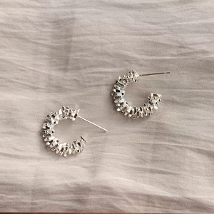Macro shot of silver C-shaped earrings with irregular crushed texture on grey fabric