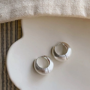 Close-up of matte brushed silver hoop earrings on a decorative ceramic tray