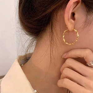 Close-up of golden textured hoop earrings showing unique woven surface on female model