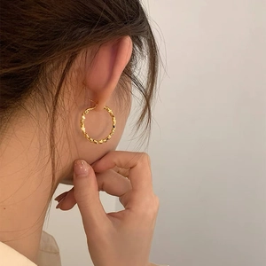 Detailed view of textured gold hoop earrings with granular pattern on a model