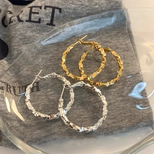 Detailed view of large gold and silver hoop earrings with unique geometric block texture