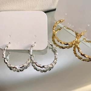Close-up of gold and silver hoop earrings with a faceted geometric mosaic texture design
