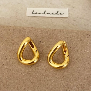 Macro shot of gold teardrop twist earrings with high-shine metallic finish on a textured base