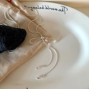 Detail of silver bow necklace with long tassels and teardrop pendants on ceramic plate
