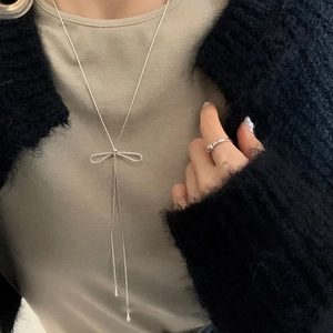 Detail view of long silver tassel necklace with bow pendant on a knit sweater