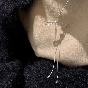 Detailed view of silver bow-shaped Y-necklace with long tassels on textured fabric