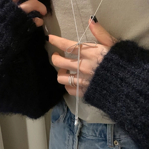 Detail of silver bow pendant with long tassels and layered rings on model