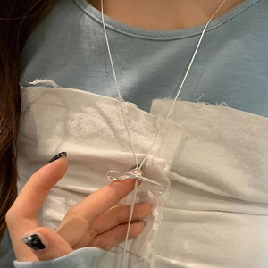 Close-up of minimalist silver bow pendant necklace with long tassel on a model