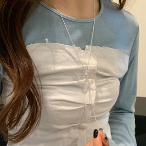 Detail shot of a silver bow necklace with long tassels worn by a model on a blue top