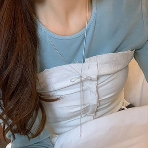 Detail of silver long tassel necklace with a bow pendant worn by a model in a blue outfit