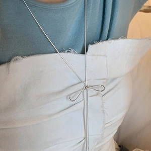 Detail of silver long tassel necklace with bow pendant worn on a minimalist blue outfit