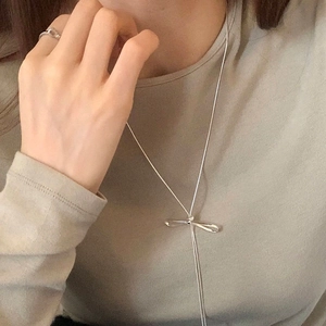 Close-up of minimalist silver bow pendant and matching open ring set on model