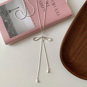 Detail of silver bow necklace featuring long fringe tassels and teardrop pendants