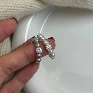 Detailed view of pearl bead rings with square zircon accents on neutral fabric background