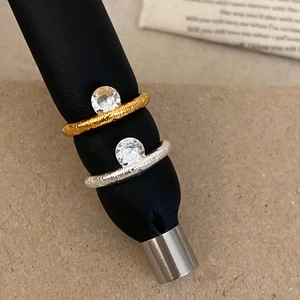 Textured gold and silver rings with round cubic zirconia stones on black leather stands