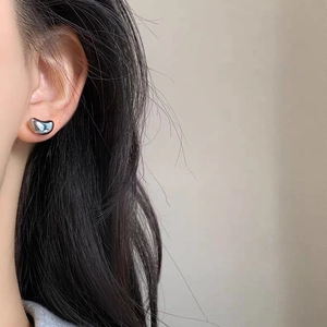 Minimalist silver bean-shaped stud earrings in polished metal on a female model
