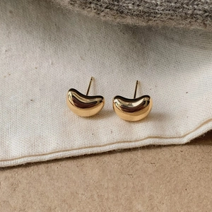 Detailed close-up of bean-shaped gold stud earrings on soft fabric background
