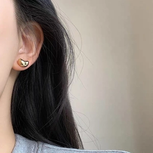 Macro side view of a model wearing minimalist polished gold bean stud earrings
