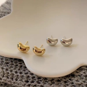 Close-up of gold and silver bean-shaped earrings on a white ceramic tray with soft lighting