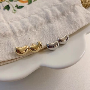 Detailed close-up of bean-shaped metal stud earrings in gold and silver finishes