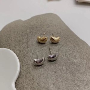 Detailed view of two pairs of bean-shaped earrings in polished gold and silver finishes