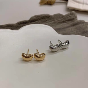 Macro view of minimalist bean-shaped stud earrings in polished gold and silver finishes