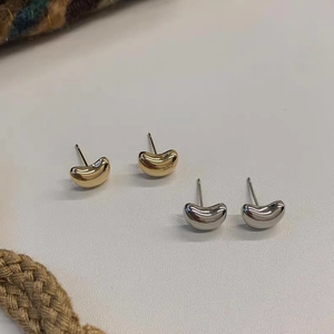 Detailed close-up of minimalist bean-shaped stud earrings in polished gold and silver finish