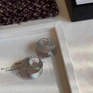 Silver-toned layered wave earrings with textured folding design on beige display tray