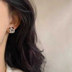Close-up of twisted knot silver stud earring worn on ear with minimalist metal design