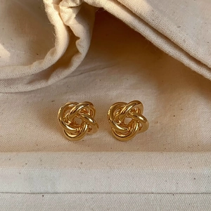 Close-up of golden twist knot stud earrings on a textured fabric background