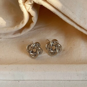 Detailed view of silver knot stud earrings on a textured fabric background