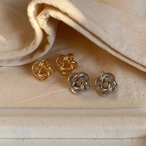Detail shot of gold and silver twisted knot stud earrings on a beige linen fabric