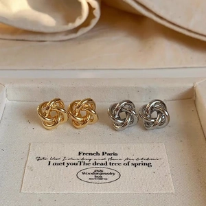 Close-up of gold and silver twisted knot stud earrings on a beige texture display