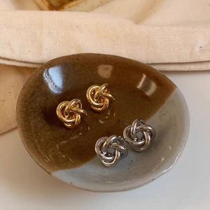 Detail of twisted knot earrings in gold and silver finish on a ceramic plate