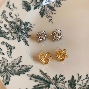Detailed close-up of gold and silver knot stud earrings on a vintage floral porcelain plate