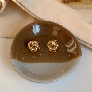 Close-up of golden twisted knot stud earrings on a minimalist ceramic plate display