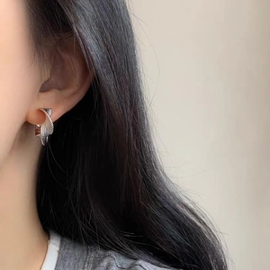 Silver twisted Mobius hoop earrings with textured finish on female model's ear