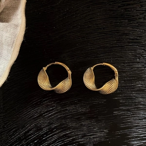 Detailed close-up of golden Mobius twist earrings with braided texture on dark wood